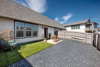 A house with a grey roof and a white exterior is shown with a patio area in front.